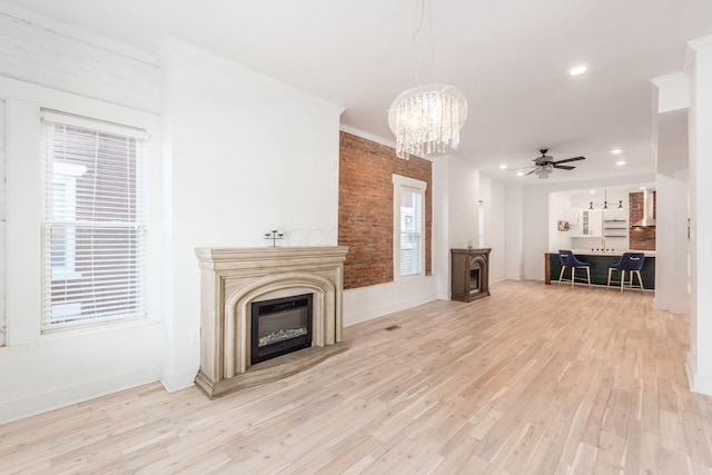 unfurnished living room featuring ceiling fan with notable chandelier, crown molding, and light hardwood / wood-style flooring