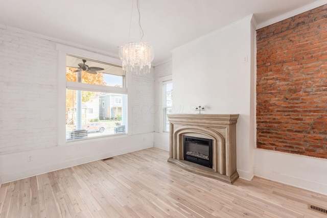 unfurnished living room with ceiling fan with notable chandelier, ornamental molding, brick wall, and light hardwood / wood-style flooring