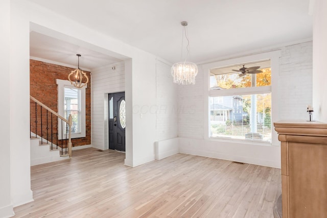 unfurnished dining area with ceiling fan with notable chandelier, light wood-type flooring, and brick wall