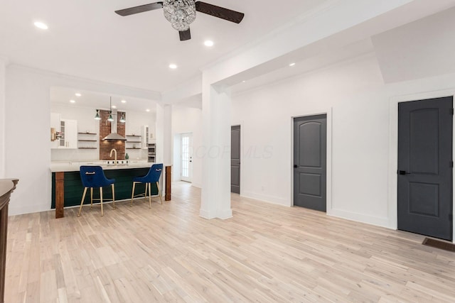 living room featuring ceiling fan, sink, crown molding, and light wood-type flooring