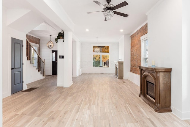 unfurnished living room featuring ceiling fan with notable chandelier, brick wall, and light hardwood / wood-style flooring