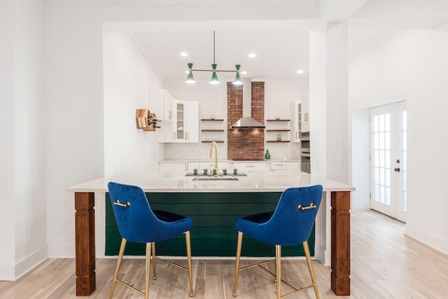 bar featuring light wood-type flooring, ornamental molding, wall chimney exhaust hood, sink, and white cabinets