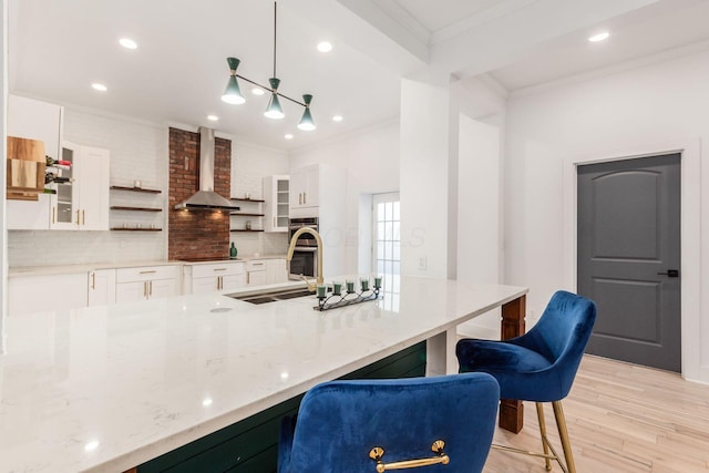 kitchen featuring white cabinetry, light wood-type flooring, wall chimney range hood, and a breakfast bar area