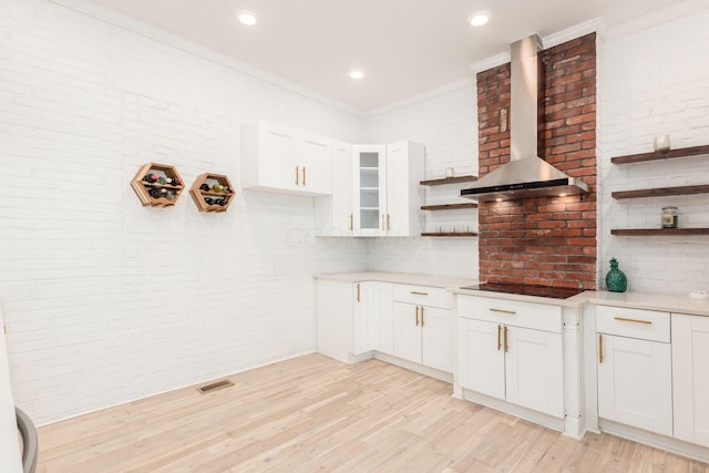 kitchen featuring white cabinets, wall chimney range hood, light hardwood / wood-style flooring, ornamental molding, and black electric cooktop