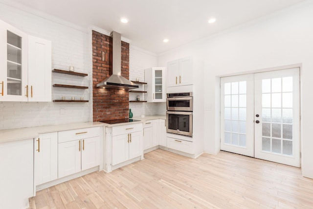 kitchen featuring white cabinetry, light hardwood / wood-style flooring, stainless steel double oven, and wall chimney range hood