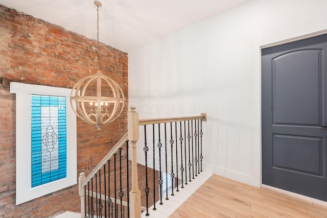 hall featuring hardwood / wood-style flooring, a notable chandelier, and brick wall