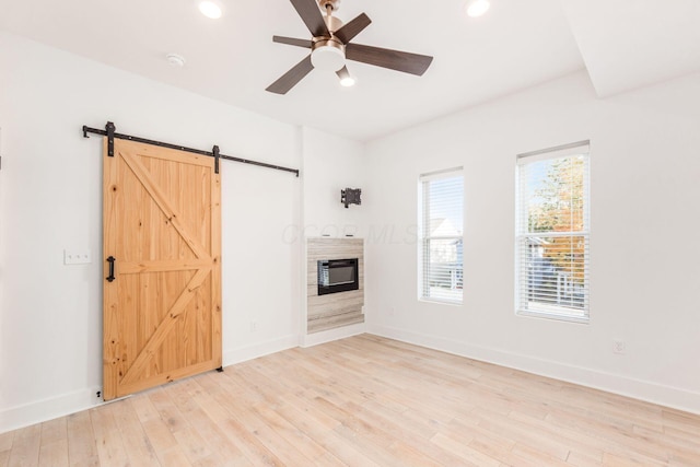 unfurnished living room with a barn door, ceiling fan, and light hardwood / wood-style flooring