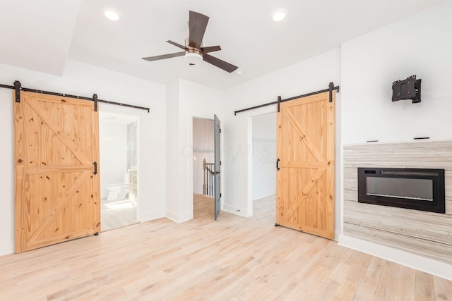 interior space with wood-type flooring, a barn door, ensuite bathroom, and ceiling fan