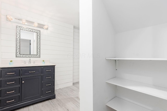 bathroom with wooden walls, vanity, and lofted ceiling