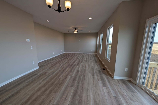 empty room with ceiling fan with notable chandelier, baseboards, wood finished floors, and recessed lighting