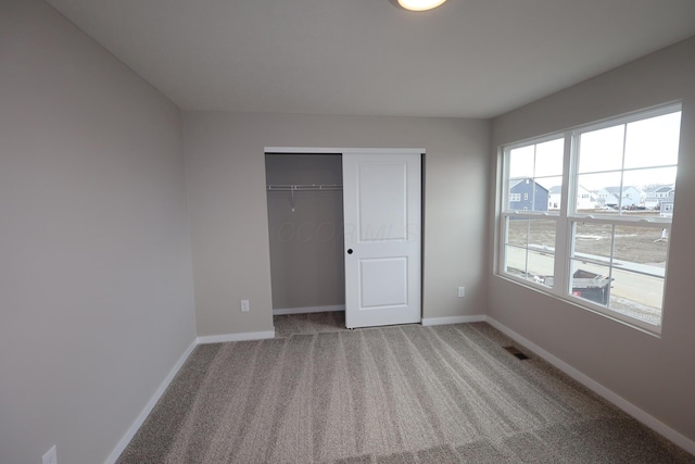 unfurnished bedroom with carpet floors, baseboards, visible vents, and a closet