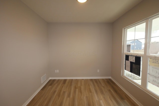 spare room featuring wood finished floors, visible vents, and baseboards