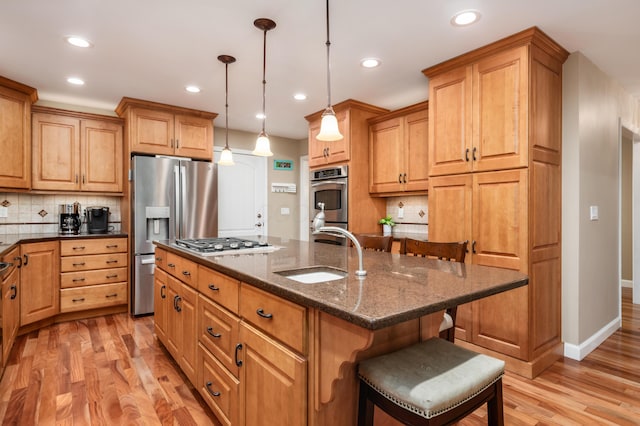 kitchen featuring pendant lighting, sink, a breakfast bar area, dark stone counters, and a center island with sink