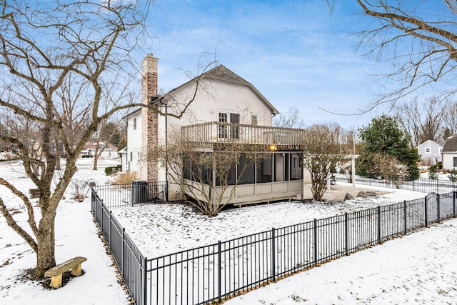 snow covered rear of property with a balcony, central AC unit, and a sunroom