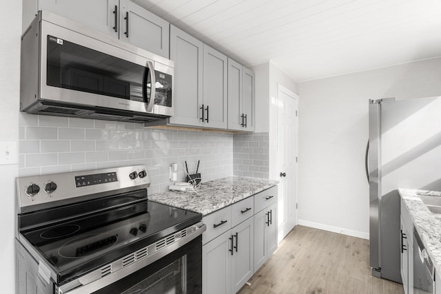 kitchen with decorative backsplash, light stone countertops, appliances with stainless steel finishes, and light hardwood / wood-style flooring