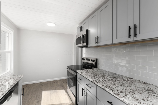 kitchen with gray cabinetry, light stone countertops, stainless steel appliances, and light hardwood / wood-style floors