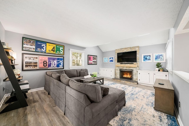 living room featuring lofted ceiling, a stone fireplace, wood-type flooring, and a textured ceiling