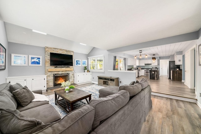 living room featuring light hardwood / wood-style floors, a stone fireplace, and lofted ceiling