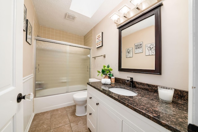 full bathroom with combined bath / shower with glass door, tile patterned floors, vanity, a textured ceiling, and toilet