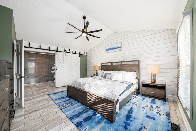 bedroom featuring ceiling fan, a barn door, light hardwood / wood-style flooring, wood walls, and lofted ceiling