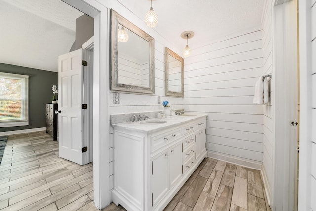 bathroom with hardwood / wood-style flooring, vanity, wood walls, and a textured ceiling