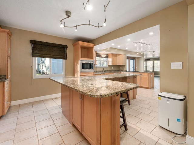 kitchen featuring a spacious island, a breakfast bar area, light stone counters, light brown cabinets, and stainless steel microwave