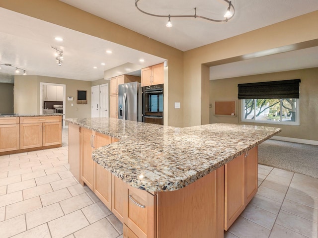 kitchen featuring double oven, stainless steel fridge, light stone counters, and a spacious island