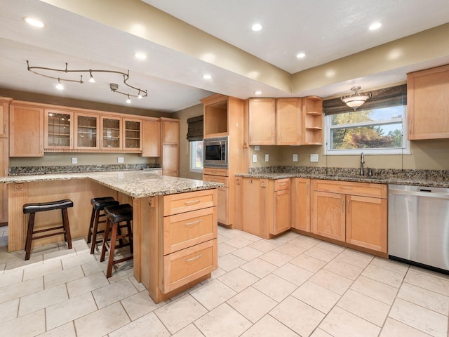 kitchen with sink, stainless steel appliances, a center island, light stone counters, and a kitchen bar