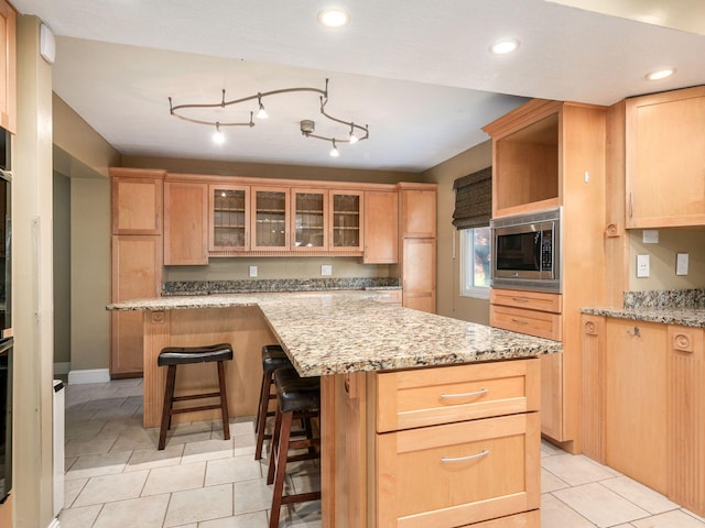 kitchen with light tile patterned floors, a kitchen breakfast bar, a center island, stainless steel microwave, and light stone counters