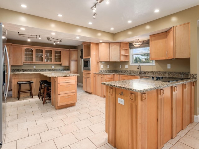 kitchen with sink, a breakfast bar area, a center island, stainless steel appliances, and light stone countertops