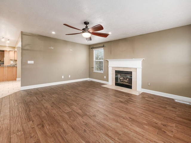 unfurnished living room featuring ceiling fan, a fireplace, hardwood / wood-style floors, and a textured ceiling