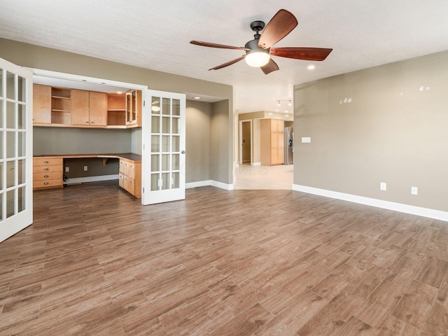 unfurnished living room featuring french doors, ceiling fan, built in desk, and light hardwood / wood-style floors