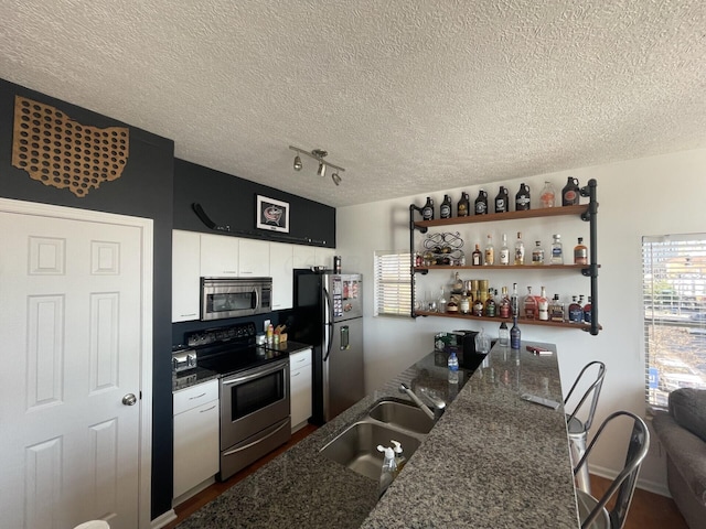 kitchen with dark wood-type flooring, sink, dark stone countertops, a textured ceiling, and appliances with stainless steel finishes