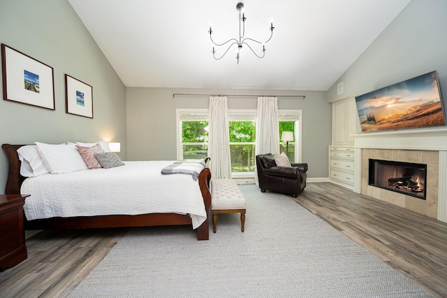 bedroom featuring a tile fireplace, wood-type flooring, vaulted ceiling, and a notable chandelier