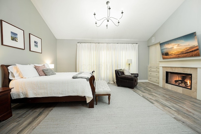 bedroom featuring a tile fireplace, hardwood / wood-style floors, an inviting chandelier, and lofted ceiling