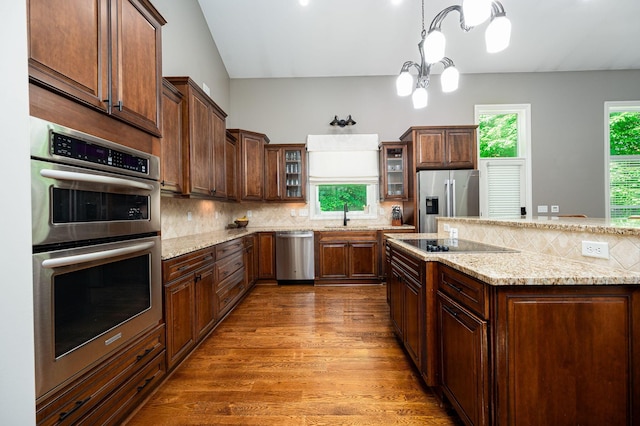 kitchen featuring a notable chandelier, hardwood / wood-style floors, pendant lighting, decorative backsplash, and appliances with stainless steel finishes