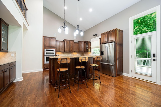 kitchen featuring light stone counters, a center island, high vaulted ceiling, and appliances with stainless steel finishes