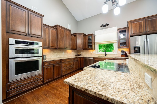 kitchen featuring sink, dark wood-type flooring, stainless steel appliances, tasteful backsplash, and light stone counters