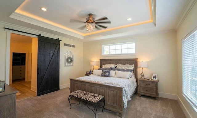 carpeted bedroom with a tray ceiling, a barn door, and multiple windows