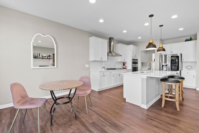 kitchen with a kitchen island with sink, dark wood-type flooring, wall chimney range hood, decorative light fixtures, and stainless steel appliances