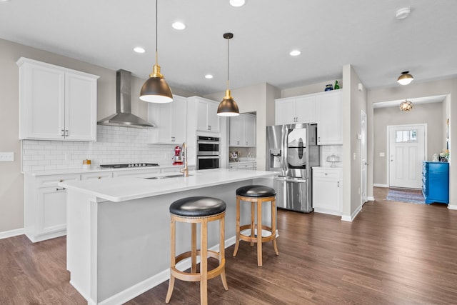 kitchen featuring dark wood-type flooring, stainless steel appliances, white cabinets, and wall chimney exhaust hood