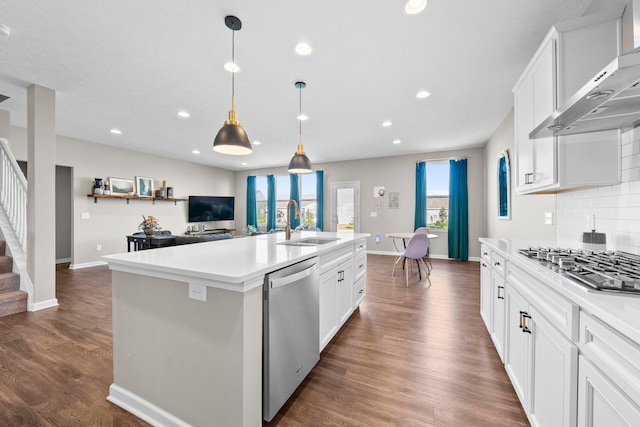 kitchen featuring wall chimney exhaust hood, white cabinets, an island with sink, and appliances with stainless steel finishes