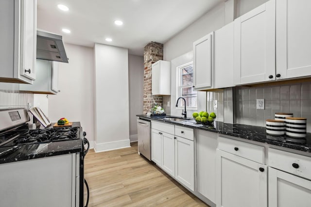 kitchen with white cabinetry, stainless steel appliances, wall chimney range hood, dark stone countertops, and light hardwood / wood-style floors