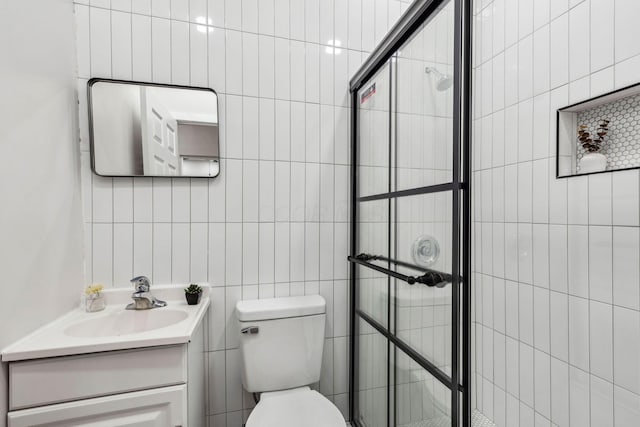 bathroom featuring toilet, vanity, tile walls, and tiled shower