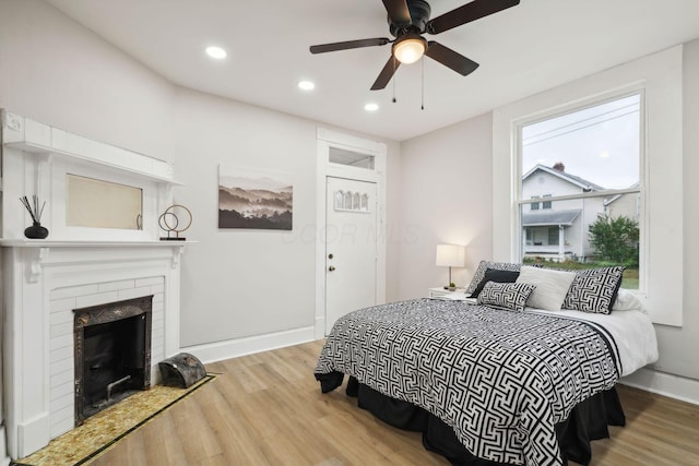 bedroom featuring hardwood / wood-style flooring, a brick fireplace, and ceiling fan