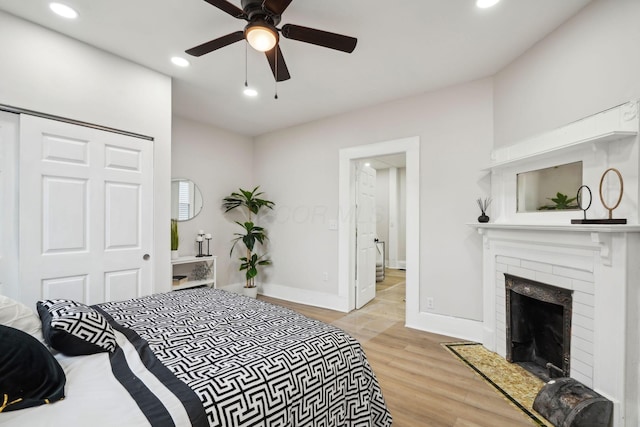 bedroom featuring a closet, a fireplace, ceiling fan, and light wood-type flooring