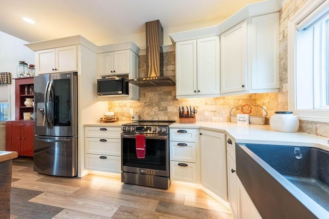 kitchen featuring white cabinets, stainless steel appliances, wall chimney exhaust hood, and light hardwood / wood-style floors