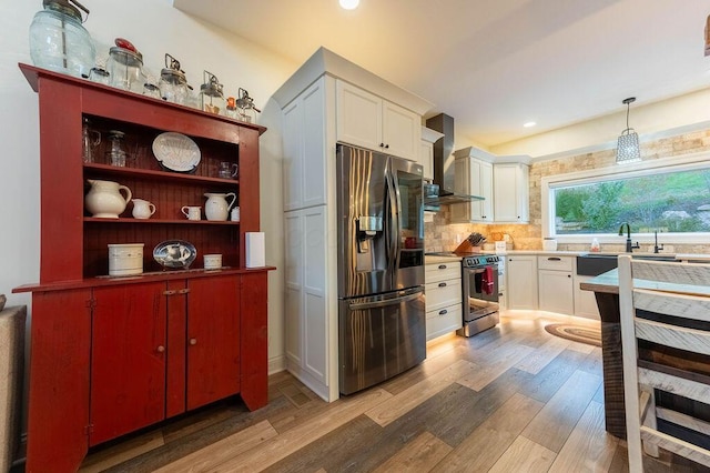 kitchen with stainless steel appliances, wall chimney range hood, pendant lighting, white cabinets, and hardwood / wood-style flooring