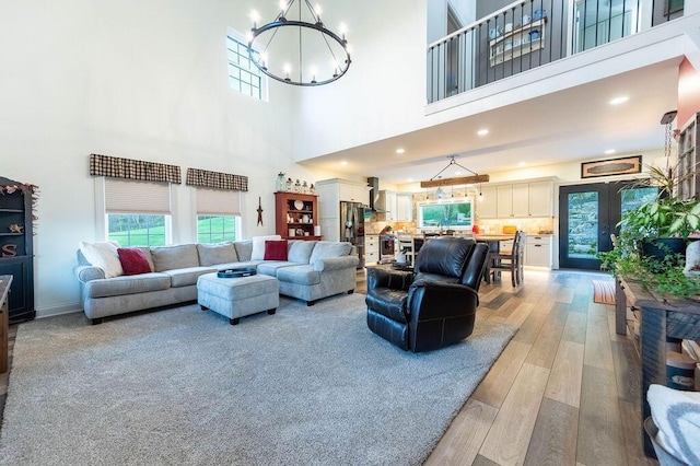 living room with a notable chandelier, light hardwood / wood-style floors, a high ceiling, and french doors