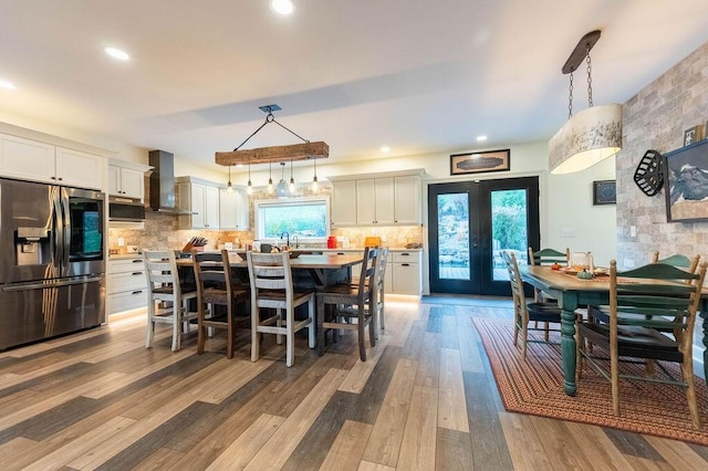 kitchen with wall chimney exhaust hood, light hardwood / wood-style floors, decorative light fixtures, and appliances with stainless steel finishes